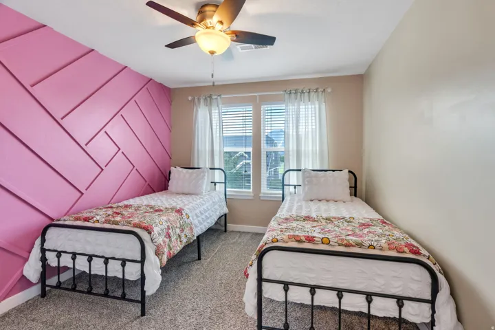 Textured accent wall, ceiling fan with integrated lighting, twin window units with blinds, and neutral wall paint
