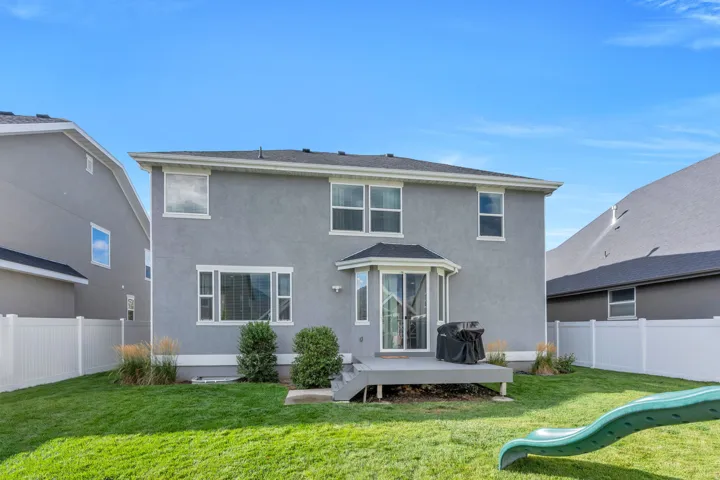 Expansive backyard featuring a manicured lawn, white vinyl fencing, and a ground-level deck with direct access to the interior