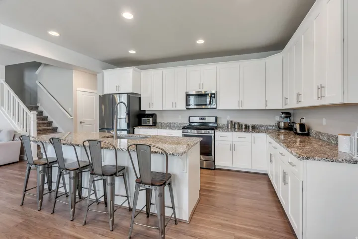 Kitchen featuring white cabinetry, granite countertops, stainless steel appliances, wood-finish flooring, and a central island with a sink