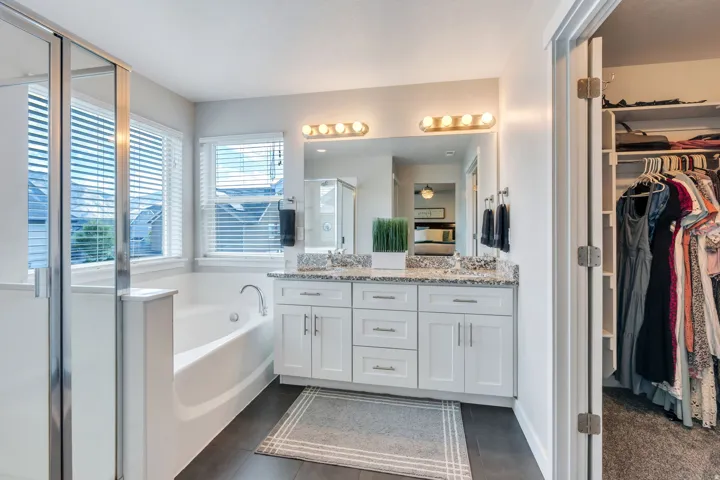 Dual-sink vanity with light-colored countertop, white cabinetry, integrated soaking tub, and a glass-enclosed shower