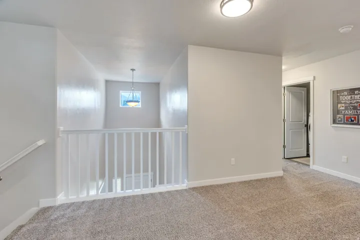Carpeted landing with white baluster railing, flush-mount ceiling light, and a prominent window