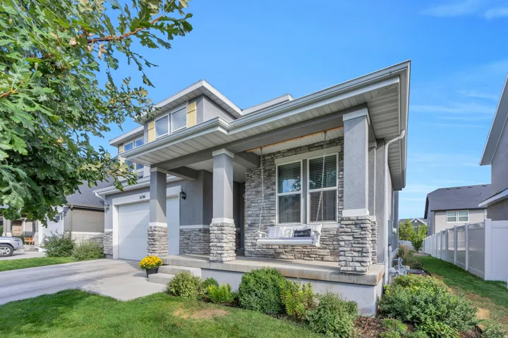 Stucco exterior with stone accents, covered front porch, attached garage, and mature landscaping