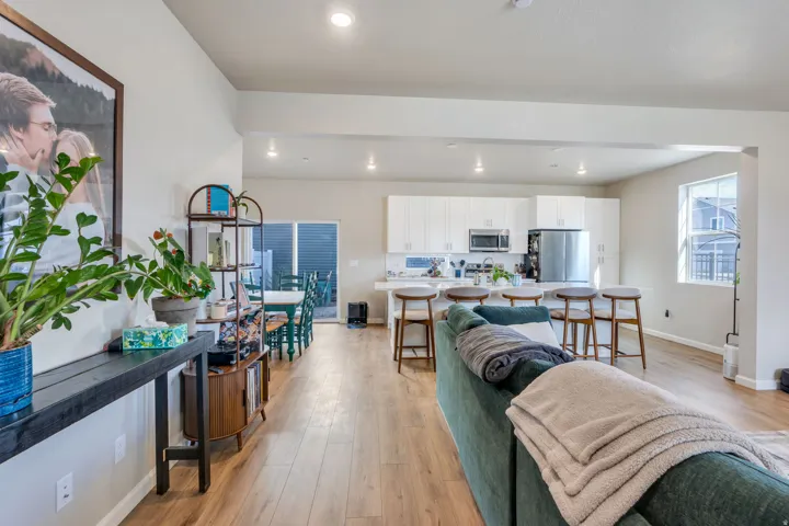 Open-concept living area featuring wood-finish flooring, recessed lighting, and a kitchen with white cabinetry and stainless steel appliances.