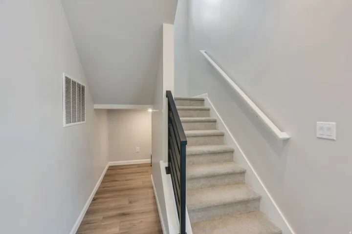 Carpeted staircase featuring a modern black metal railing and a white wall-mounted handrail. Nice little finished nook under the stairs. Perfect for a playroom or Dog area.