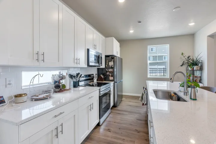 White shaker-style cabinetry with brushed nickel hardware, white subway tile backsplash, light-toned countertops, stainless steel appliances, and wood-finish flooring. Appliances to stay with home.