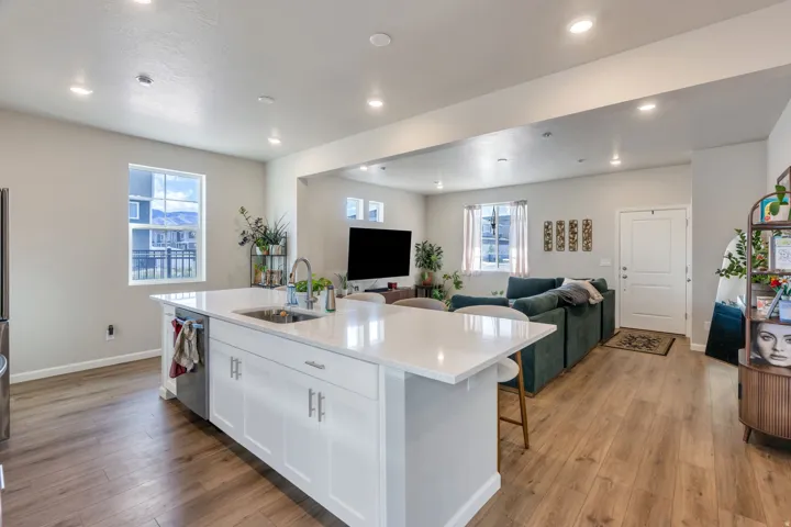 Open-concept living area featuring wood-finish flooring, recessed lighting, and a kitchen island with a built-in sink and white countertop
