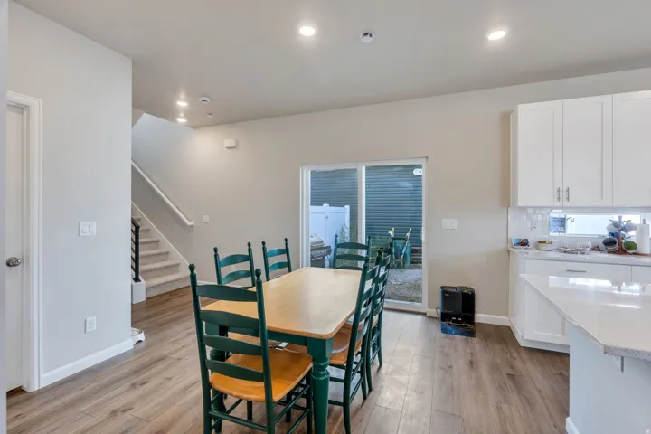Wood-finish flooring throughout, white shaker cabinetry, white subway tile backsplash, recessed lighting, and a sliding glass door to the exterior