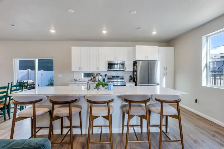 Kitchen featuring a large island with seating, white cabinetry, stainless steel appliances, and wood-finish flooring. Appliances to stay with home.
