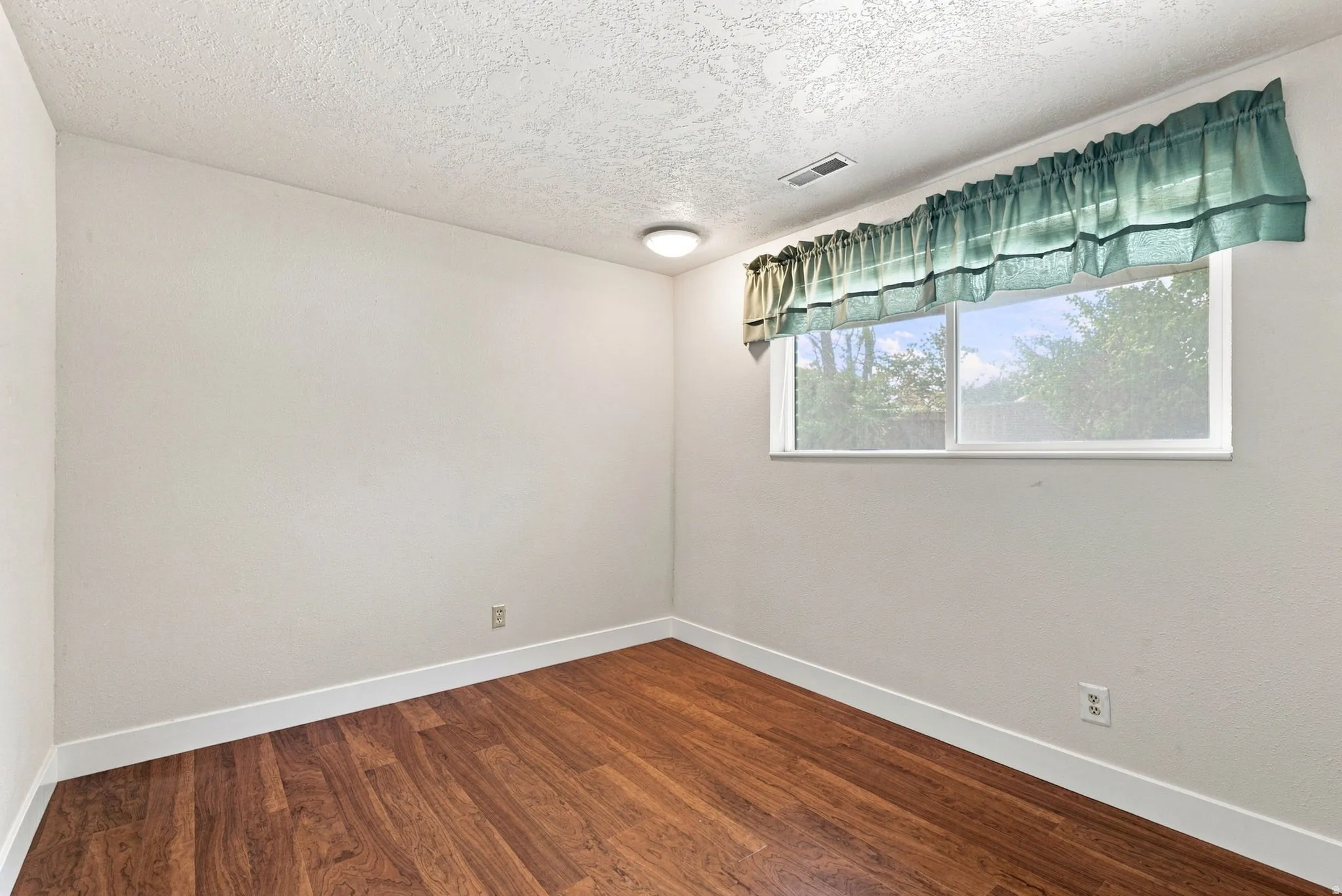 Wood-finish flooring with white trim, a single window, and a ceiling-mounted light fixture