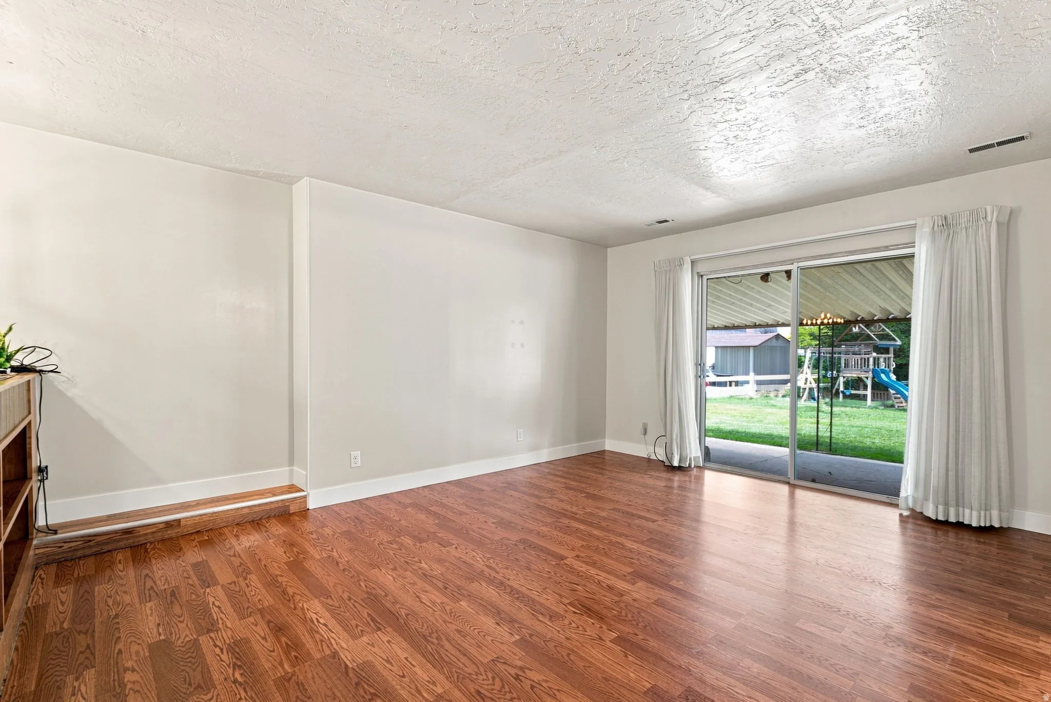 Bright, open living space showcasing gleaming wood-finish flooring, white walls, and abundant natural light from sliding glass doors