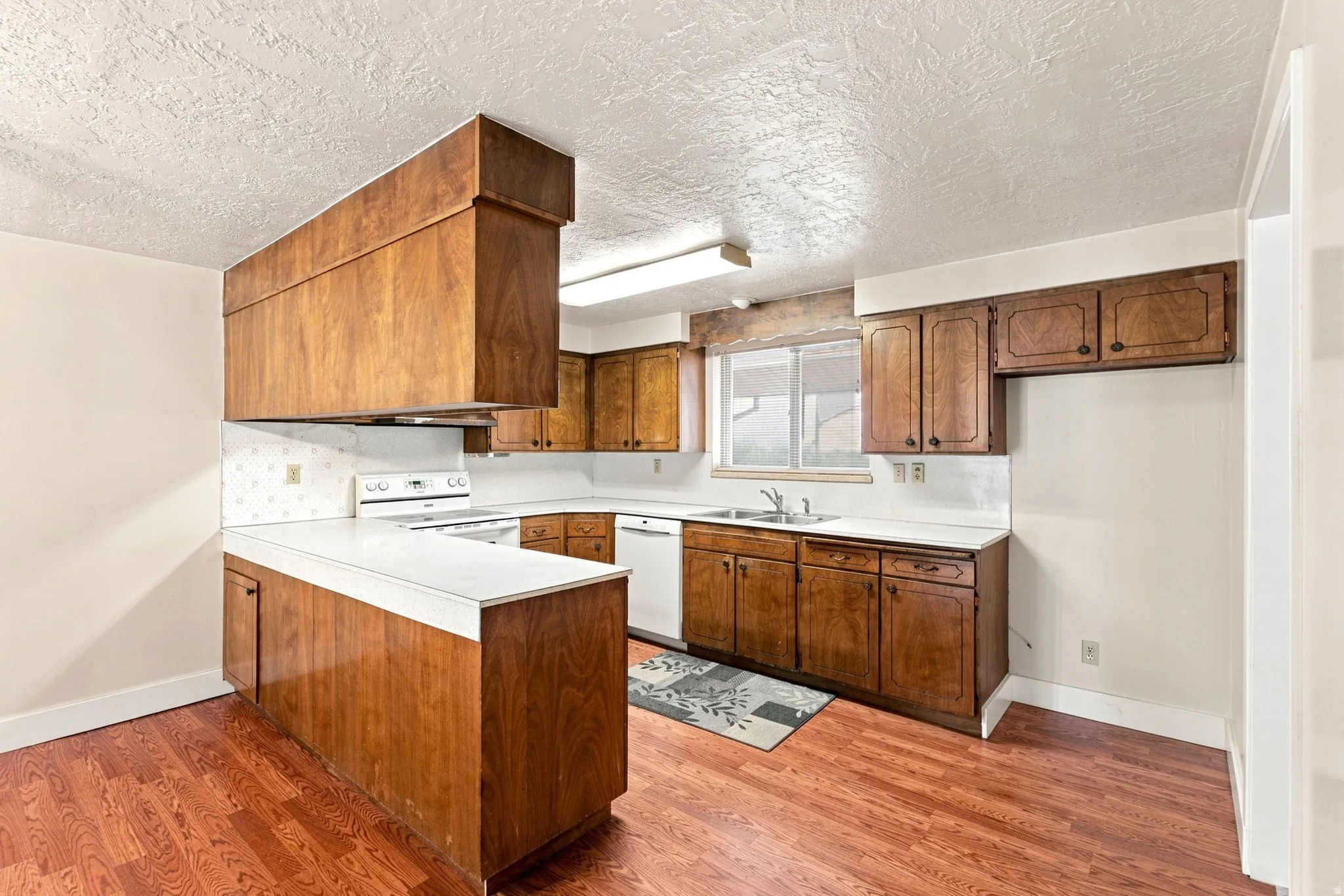 Kitchen featuring wood-finish cabinetry, white countertops, built-in white appliances, and wood-finish flooring