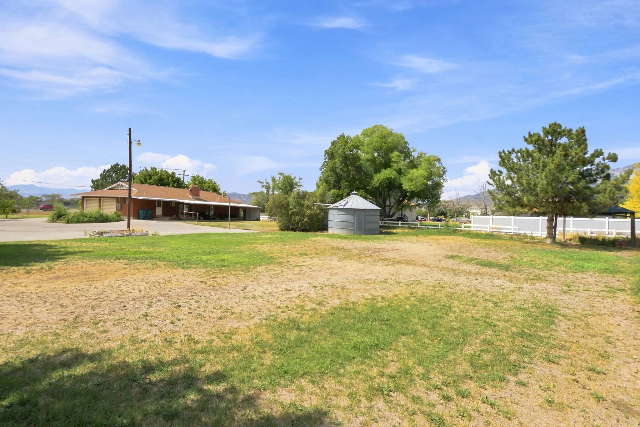 Expansive grounds featuring a detached storage silo, mature trees, white fencing, and a single-story residence with an attached garage