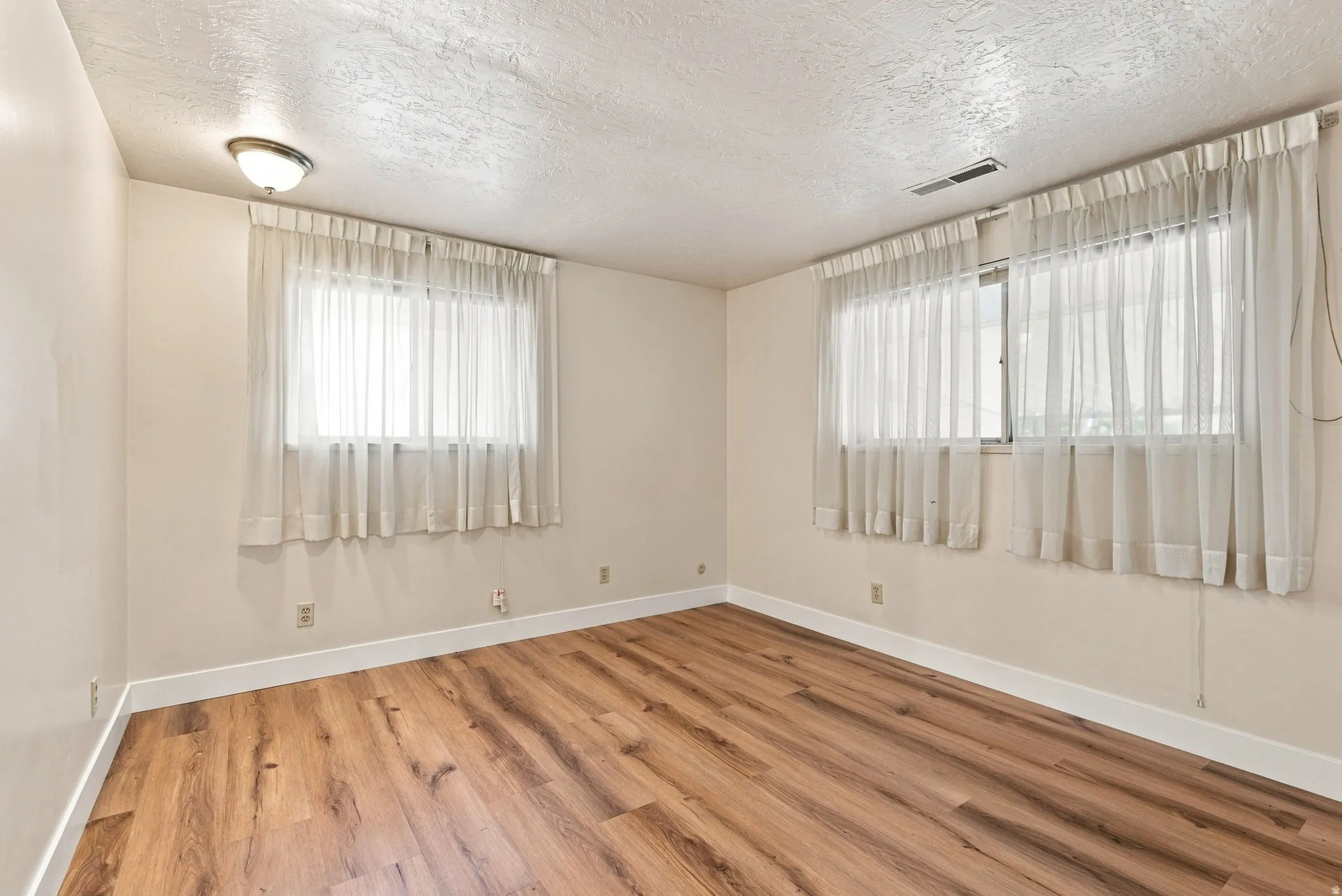 Wood-finish flooring, two windows with sheer coverings, light-toned walls, and ceiling-mounted lighting fixture