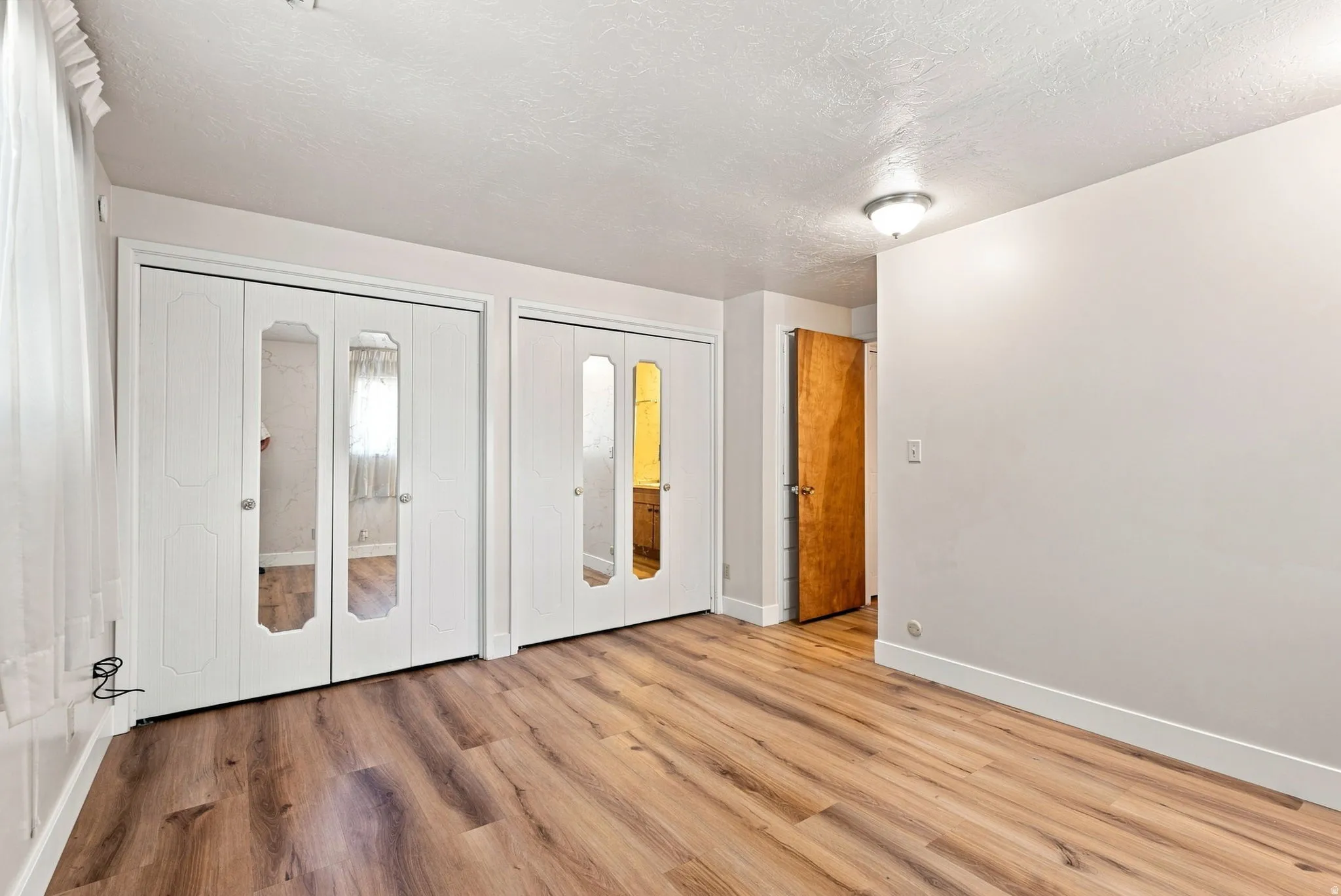 Wood-finish flooring throughout, bright white walls, and bi-fold closet doors with mirrored panels