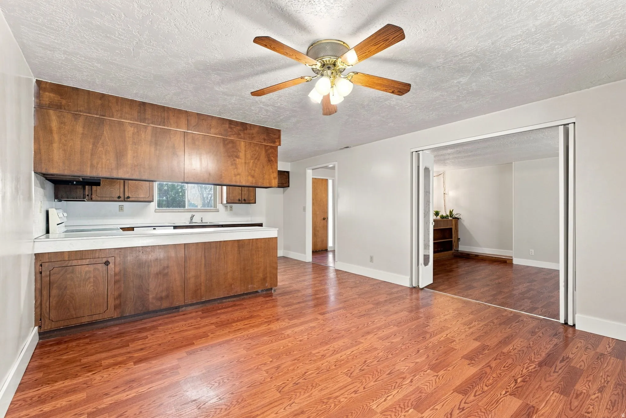 Wood-finish flooring throughout, with a ceiling fan light fixture and recessed kitchen with wood cabinetry