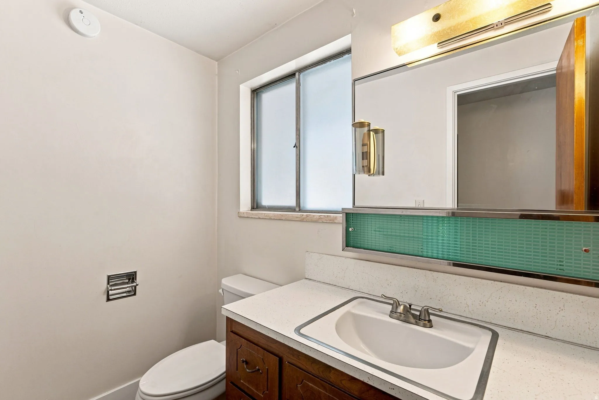 Vanity with an integrated sink, dual-handle faucet, and a large mirror with integrated lighting