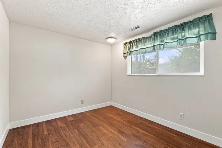 Wood-finish flooring with white trim, a single window, and a ceiling-mounted light fixture