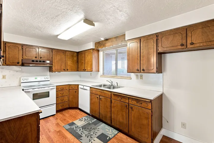 Kitchen featuring wood-finish cabinetry, white countertops, a double basin sink, and wood-finish flooring
