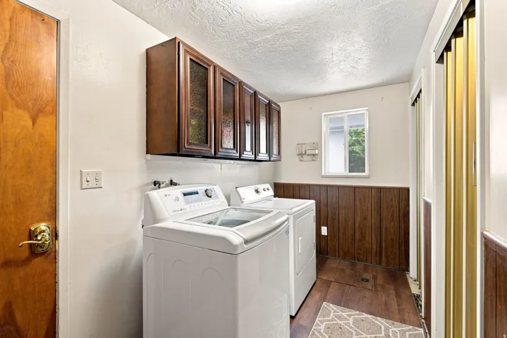Laundry area featuring wood-finish flooring, half-wall wood paneling, and upper cabinetry with glass inserts