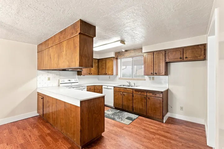 Kitchen featuring wood-finish cabinetry, white countertops, built-in white appliances, and wood-finish flooring