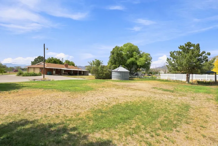 Expansive grounds featuring a detached storage silo, mature trees, white fencing, and a single-story residence with an attached garage