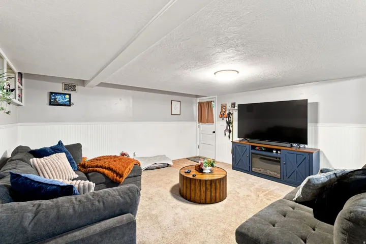 Spacious basement recreation room featuring plush seating arrangements, neutral carpet flooring, and a wood-finish entertainment center with ample storage