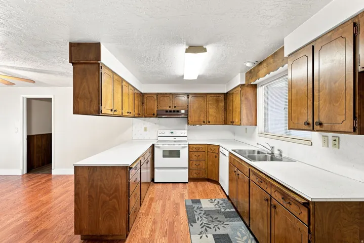 U-shaped kitchen layout featuring wood-finish cabinetry, white countertops, and a double basin stainless steel sink