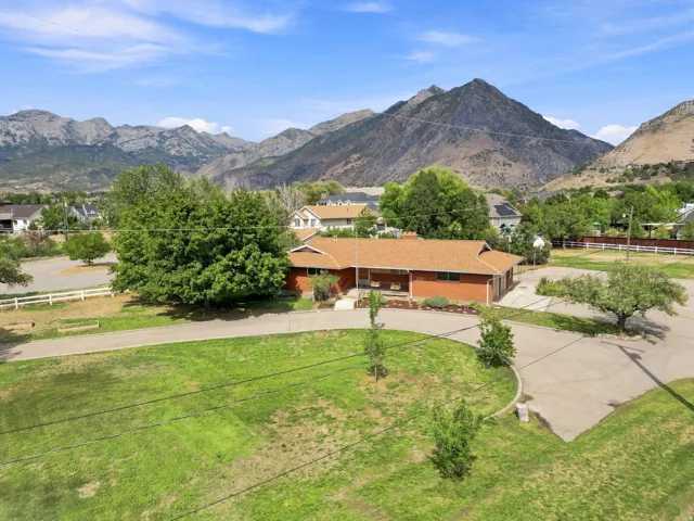 Brick-clad residence with a pitched roof, circular driveway, and mature landscaping, framed by a mountainous backdrop