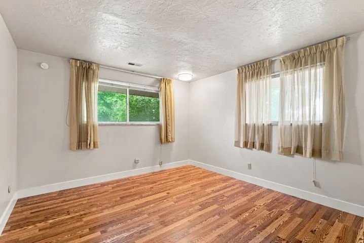 Wood-finish flooring, two windows with window treatments, light-toned wall paint, and overhead lighting