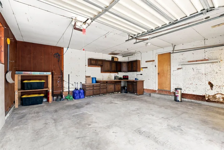 Spacious garage with concrete flooring, overhead door with automatic opener, wood-finish cabinetry, built-in workbench with storage, and exposed ceiling infrastructure