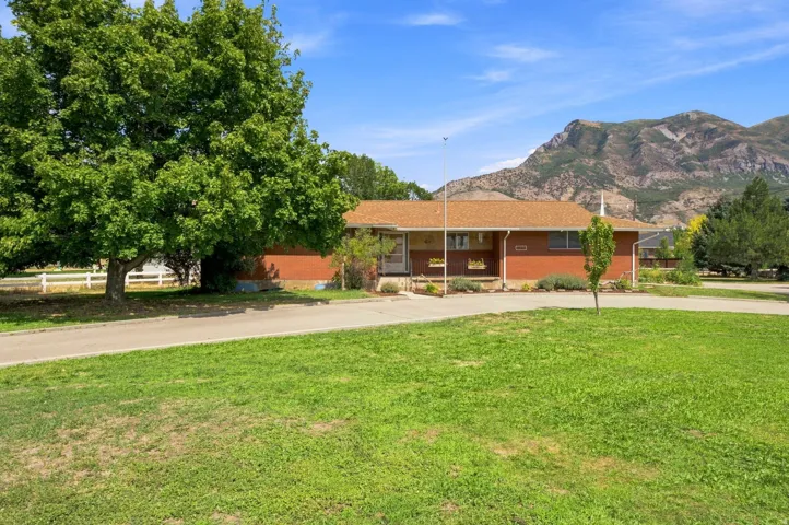 Brick exterior with a shingle roof, mature trees, a manicured lawn, and a mountain backdrop