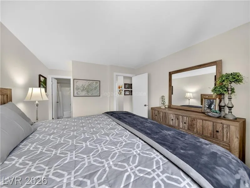 Recessed lighting, light neutral wall paint, wood-finish headboard, wood-finish dresser with dark hardware, and a large framed mirror
