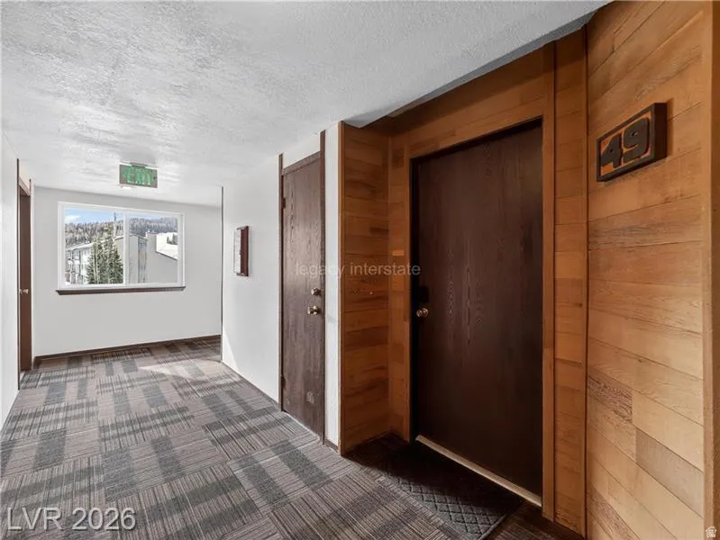 Wood-paneled wall, dark-finish entry door, patterned carpet flooring, and a white-framed window