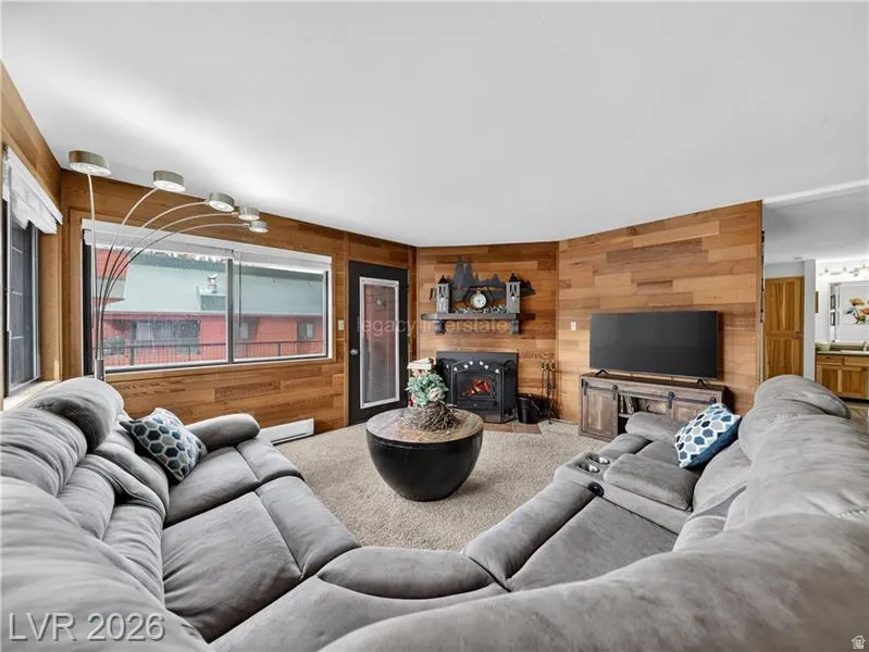 Wood paneling accent walls, fireplace with mantel, built-in media console, large windows, and an exterior door with glass insert