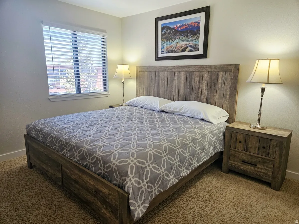 Bedroom featuring textured carpeting, window with blinds, and a wood-finish bed frame