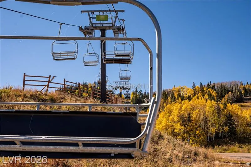 Multiple ski lifts with metal chairs, a wooden fence, and a diverse tree line featuring deciduous trees with yellow foliage and evergreen conifers