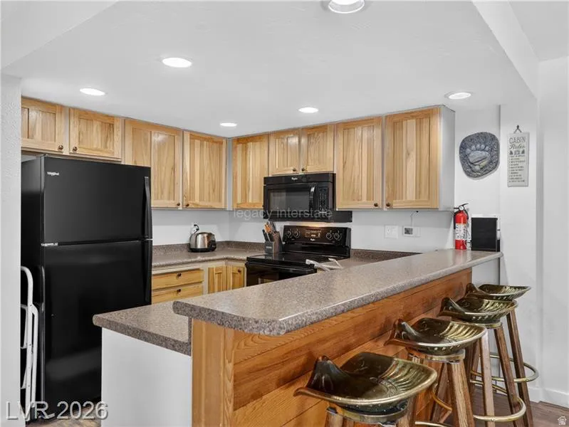 Kitchen featuring light wood cabinetry, dark countertops, a built-in black oven with stovetop, black refrigerator, and recessed lighting