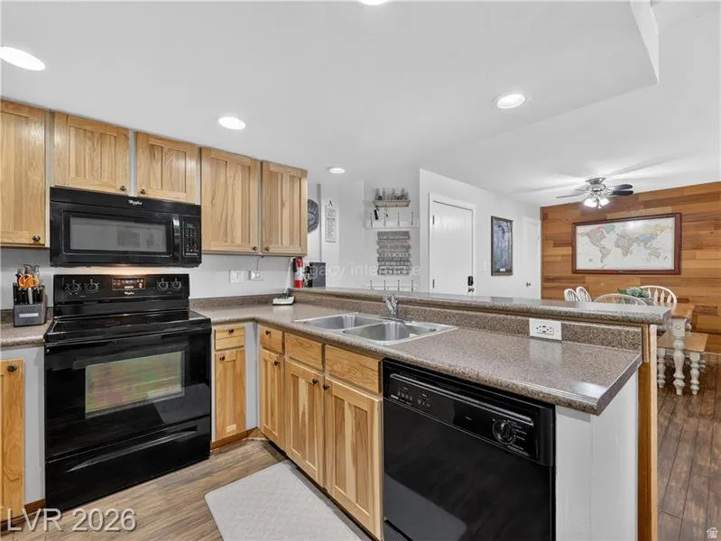 Kitchen featuring wood cabinetry, black appliances, a double basin sink, and a peninsula countertop