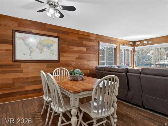 Wood-finish flooring, wood-paneled accent wall, multiple windows, and a ceiling fan with integrated lighting