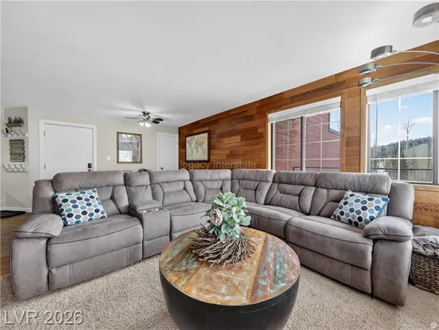 Wood-paneled accent wall, large windows, ceiling fan, and carpeted flooring