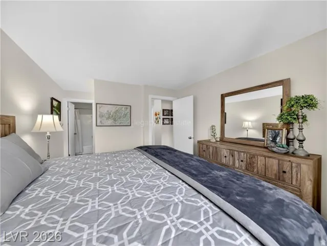 Recessed lighting, light neutral wall paint, wood-finish headboard, wood-finish dresser with dark hardware, and a large framed mirror