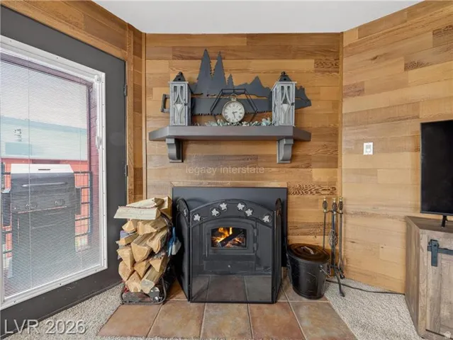 Wood paneling accent wall, fireplace with metal enclosure, tiled hearth, wood-finish flooring, and a glass-paned door