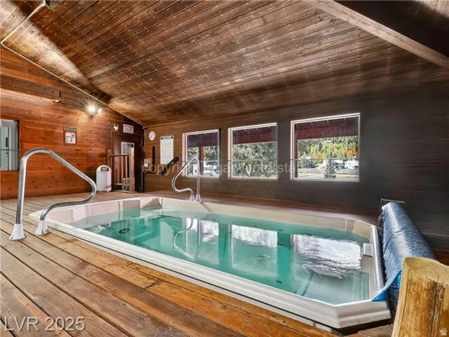Indoor hot tub with built-in grab rails, wood-finish flooring, wood-paneled walls, and a wood-slat ceiling