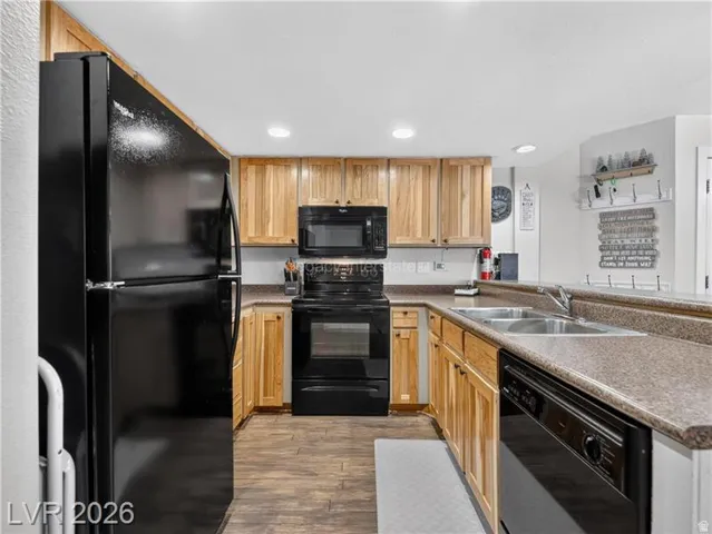 U-shaped kitchen with wood-finish flooring, light wood cabinetry, stone-finish countertops, black appliances, and recessed lighting