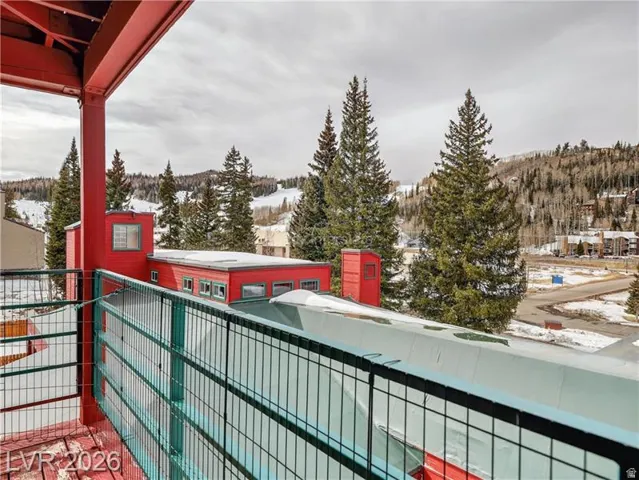 Wood-finish deck with metal railing, featuring a mountain landscape with evergreen trees