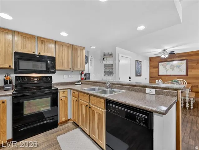 Kitchen featuring wood cabinetry, black appliances, a double basin sink, and a peninsula countertop