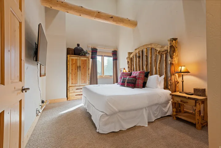 Exposed wood beam, textured wood headboard, wood-finish door, built-in wood cabinetry, and carpeted flooring