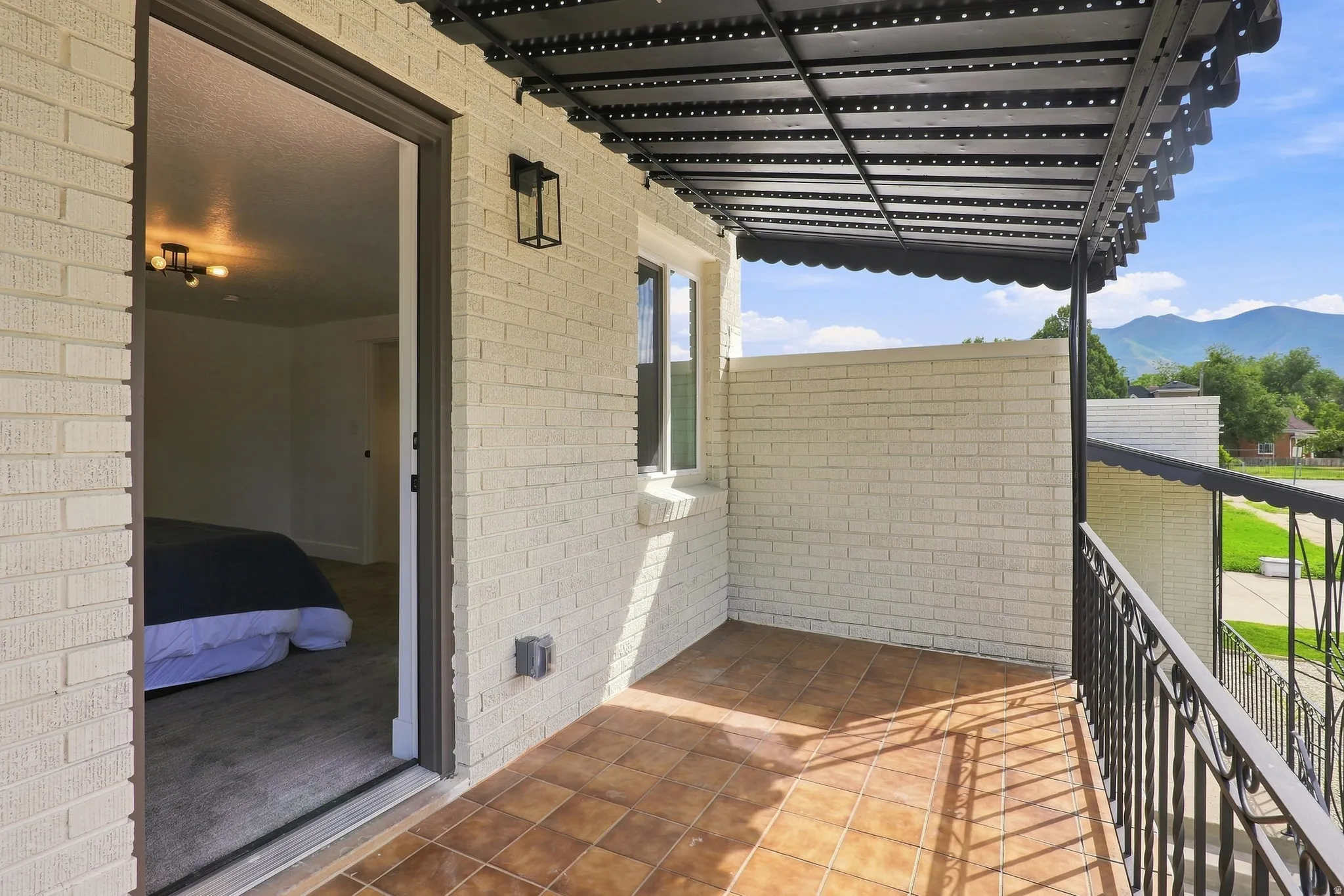 Balcony access featuring a black metal awning, decorative railing, and terra cotta-style tile flooring