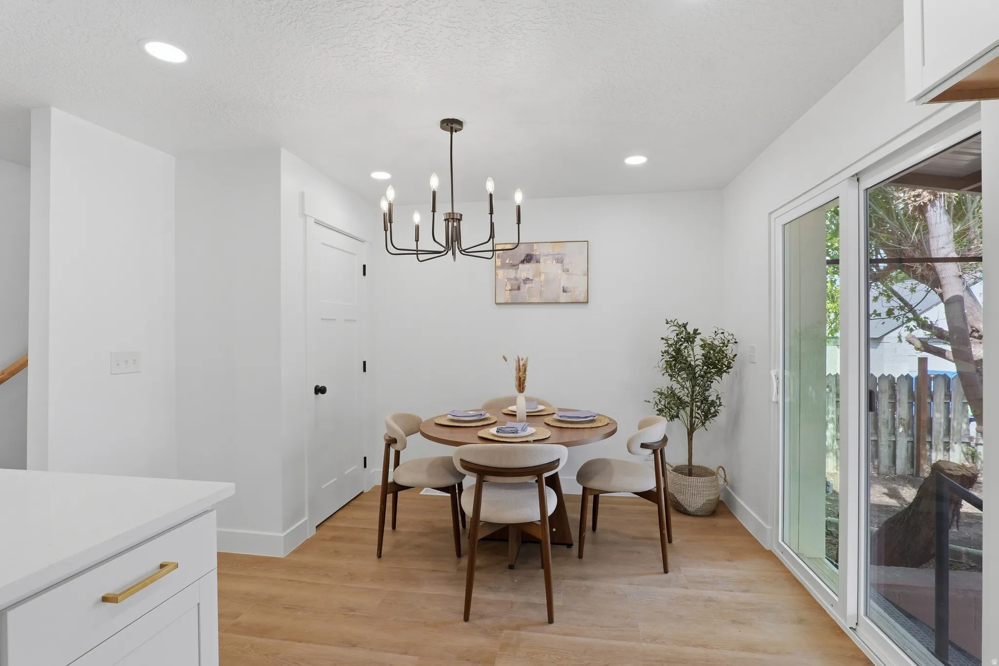 Recessed lighting, wood-finish flooring, sliding glass door, white cabinetry, and a contemporary chandelier