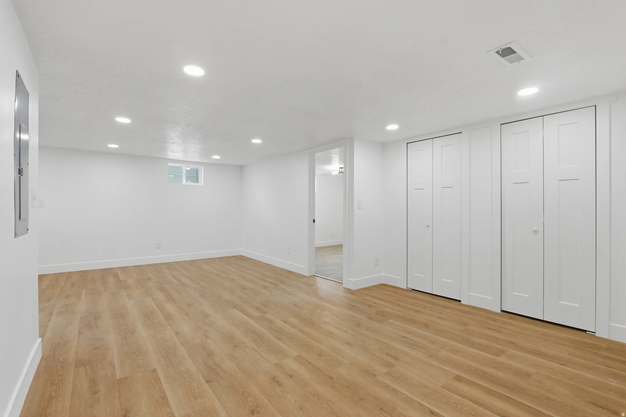 Spacious room featuring wood-finish flooring, recessed lighting, and multiple bi-fold closet doors